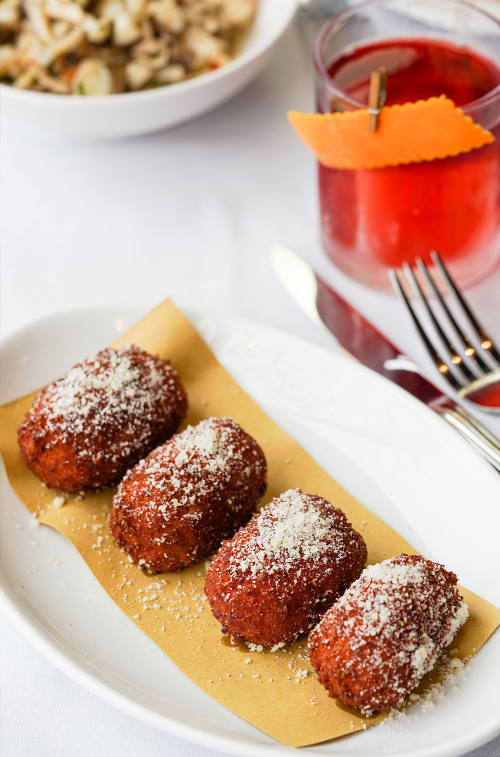 4 polpette lined on a plate next to a negroni