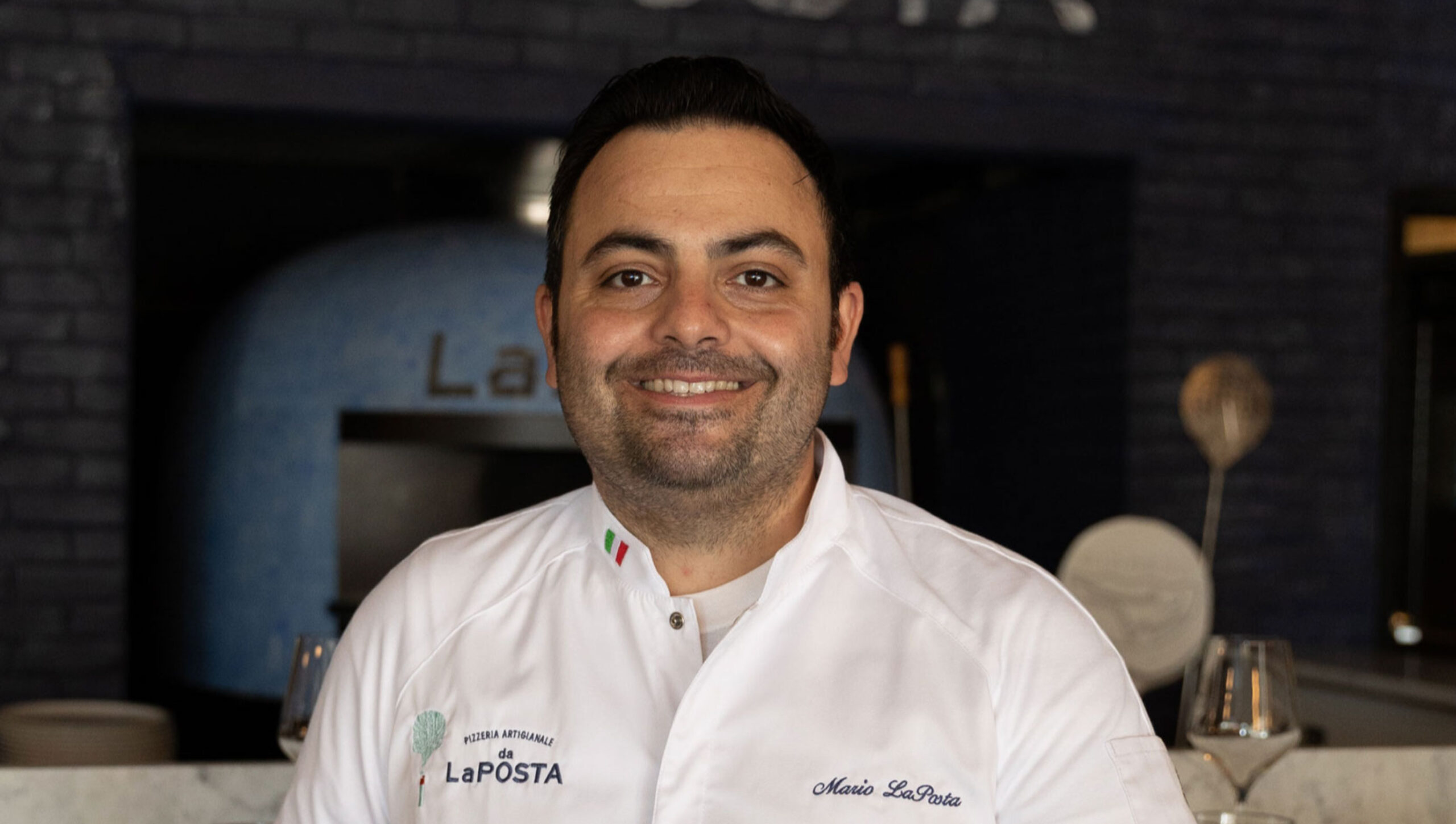 image of chef-owner mario laposta standing in front of the wood-fired pizza oven at da laposta