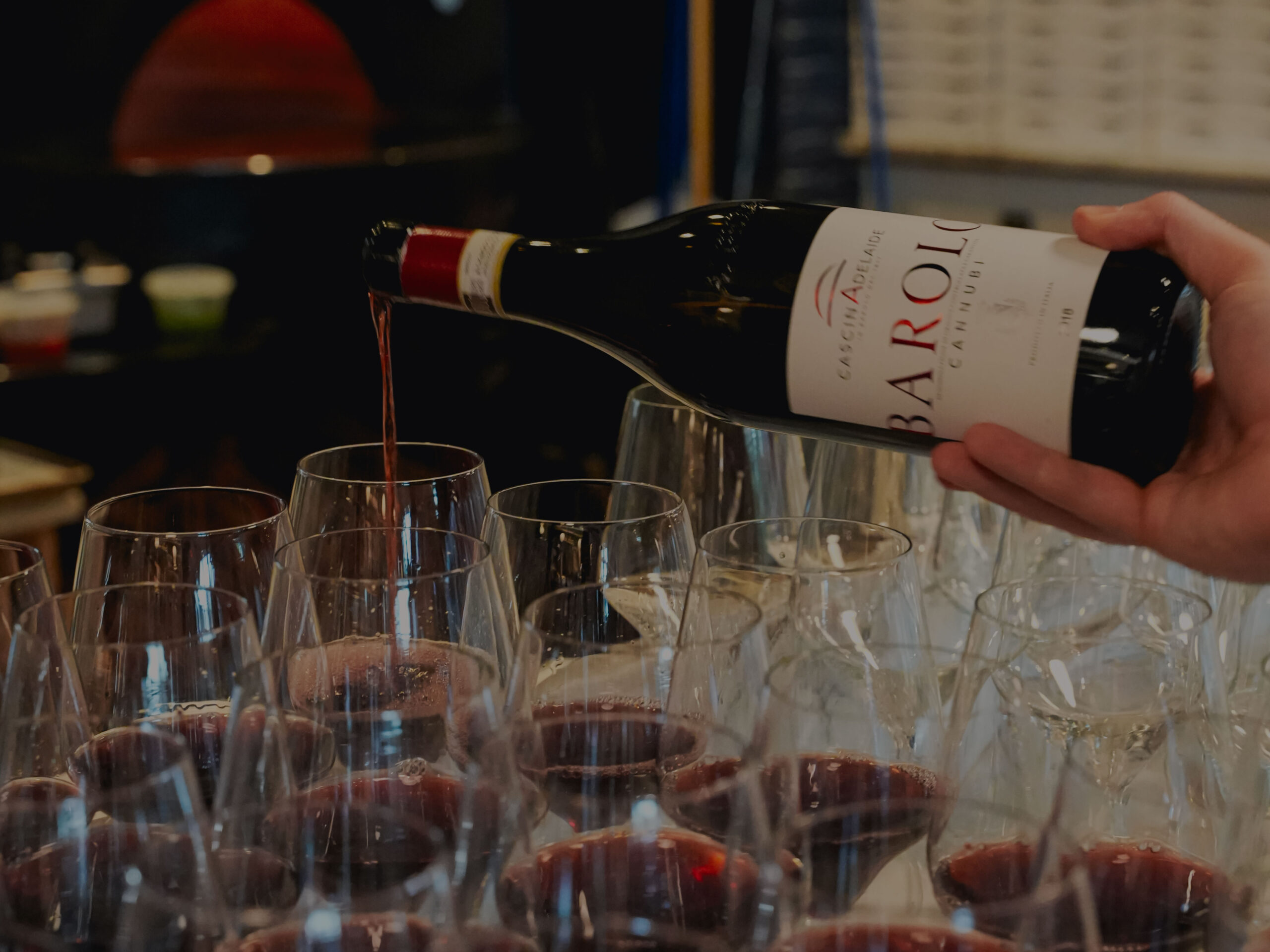 staff pouring a bottle of barolo into glass atop a table full of dozens of wine glasses
